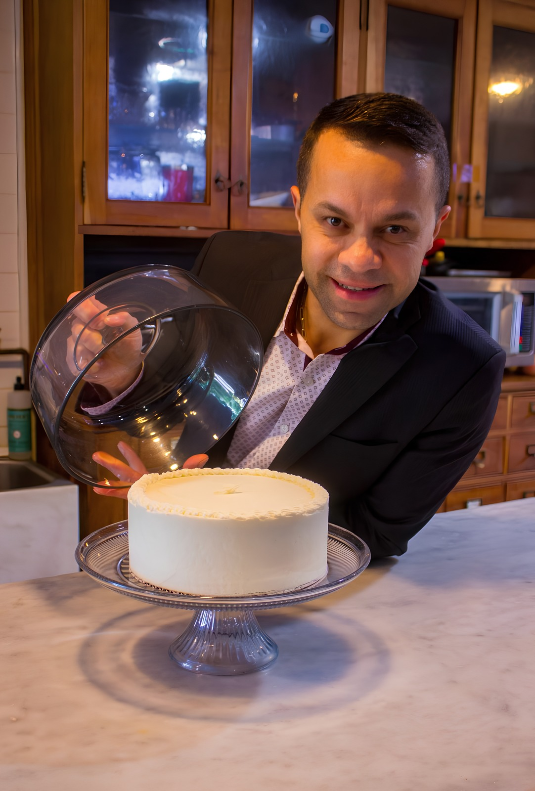 Daniel presenting a signature layer cake under a glass dome at The Market at Union Hall