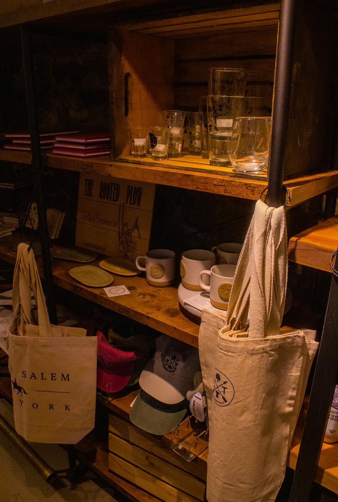 Union Hall mugs, glasses, hats, and canvas bags displayed on rustic market shelves
